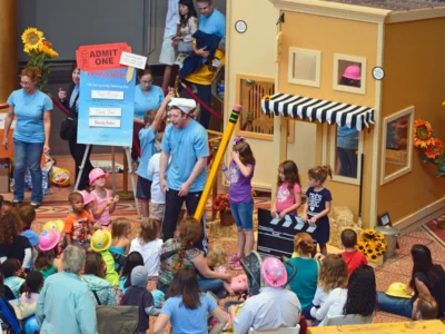 Actor entertaining group of kids in front of playhouse inside a museum.